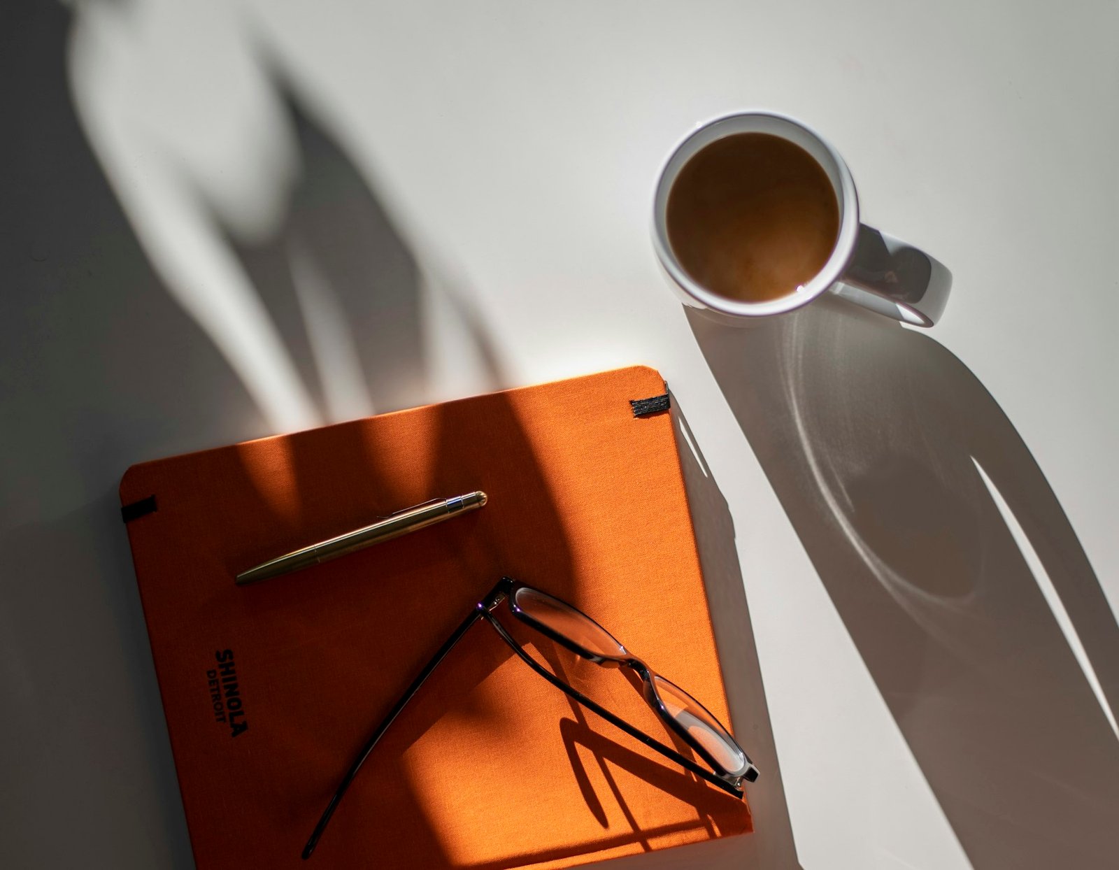 Glasses resting on an orange notebook beside coffee