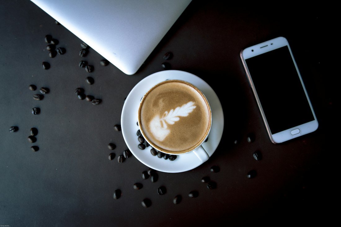 White ceramic cup on saucer beside a smartphone