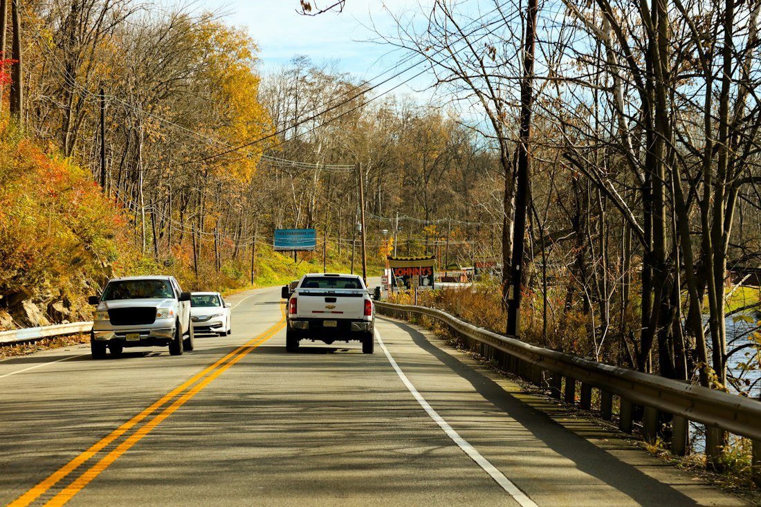 Cars driving on a road beside autumn trees