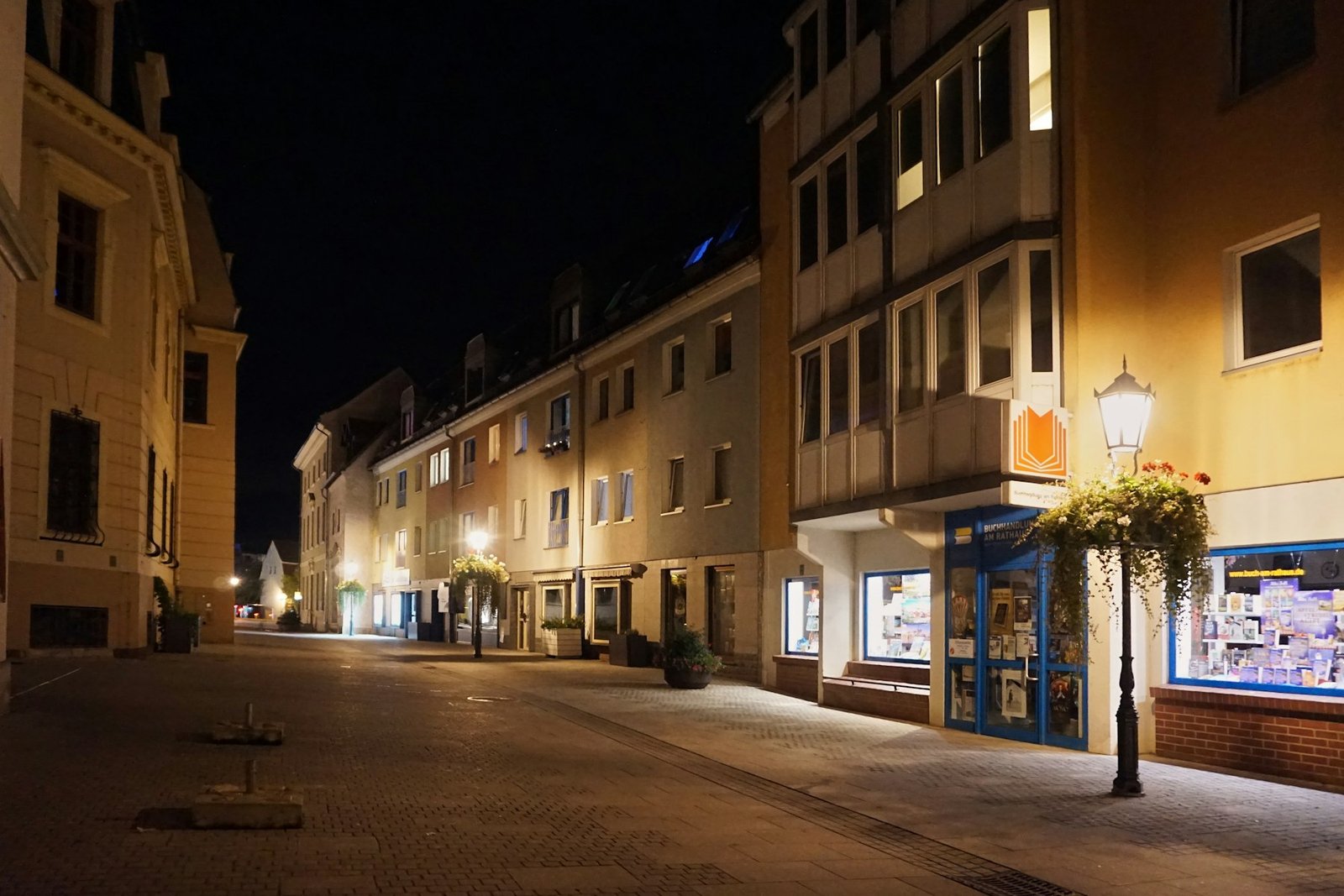 Empty street lined with illuminated buildings at night